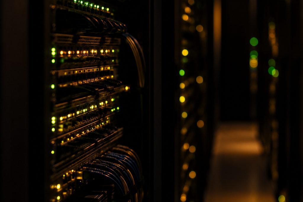 A darkened server room aisle, rows of equipment showing status lights