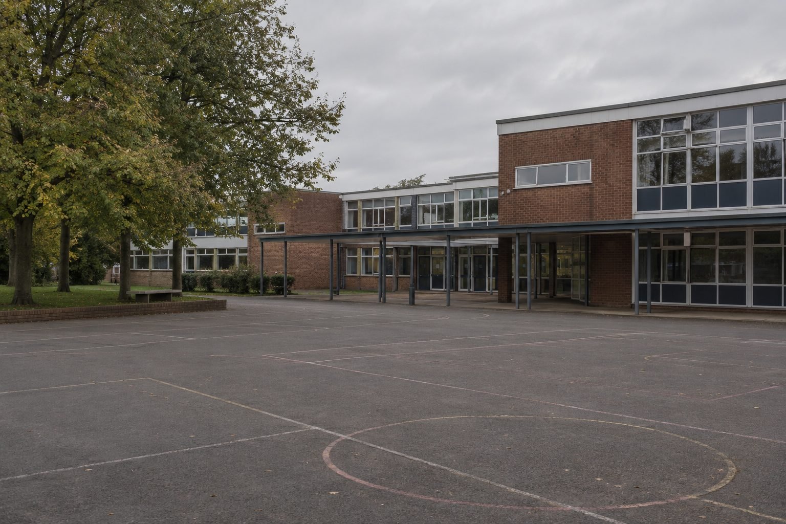 The brick and glass frontage of a British secondary school seen across an empty playground